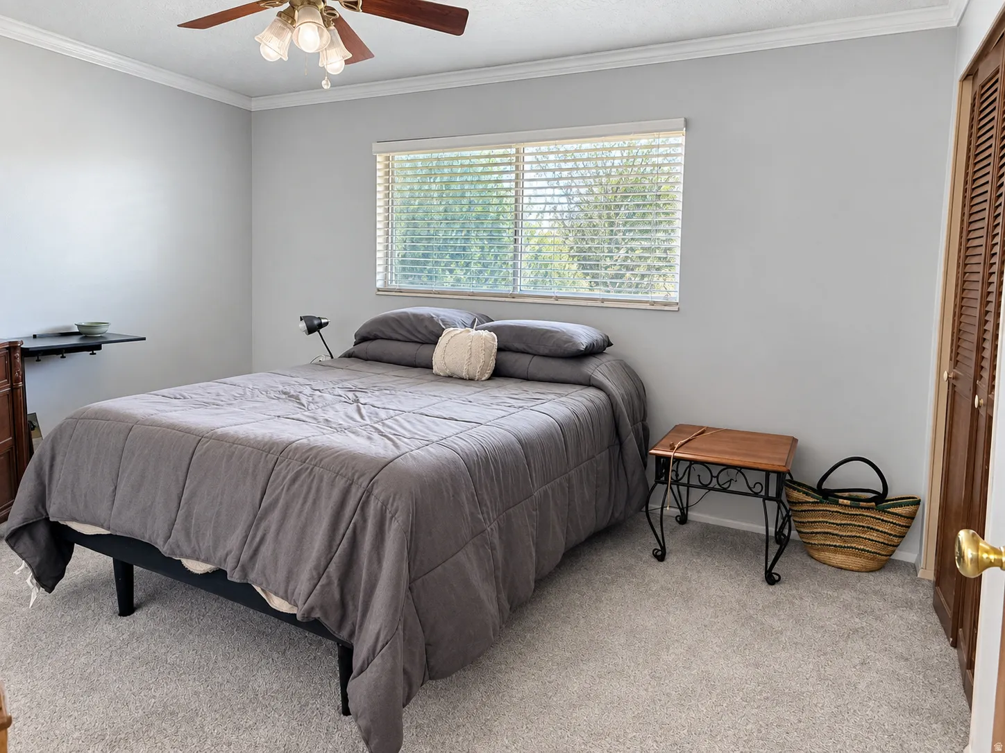 Light gray wall paint with white crown molding, a ceiling fan with light fixture, window with blinds, and light-colored carpet flooring