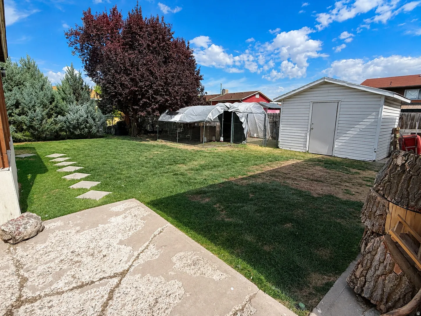 Expansive grassy yard with mature trees, a concrete patio, stepping stone pathway, and a detached storage shed