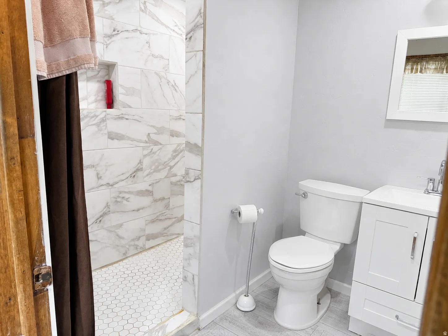 Shower with rectangular tile surrounds and hexagon tile flooring, white vanity with integrated sink, toilet, and light-colored flooring