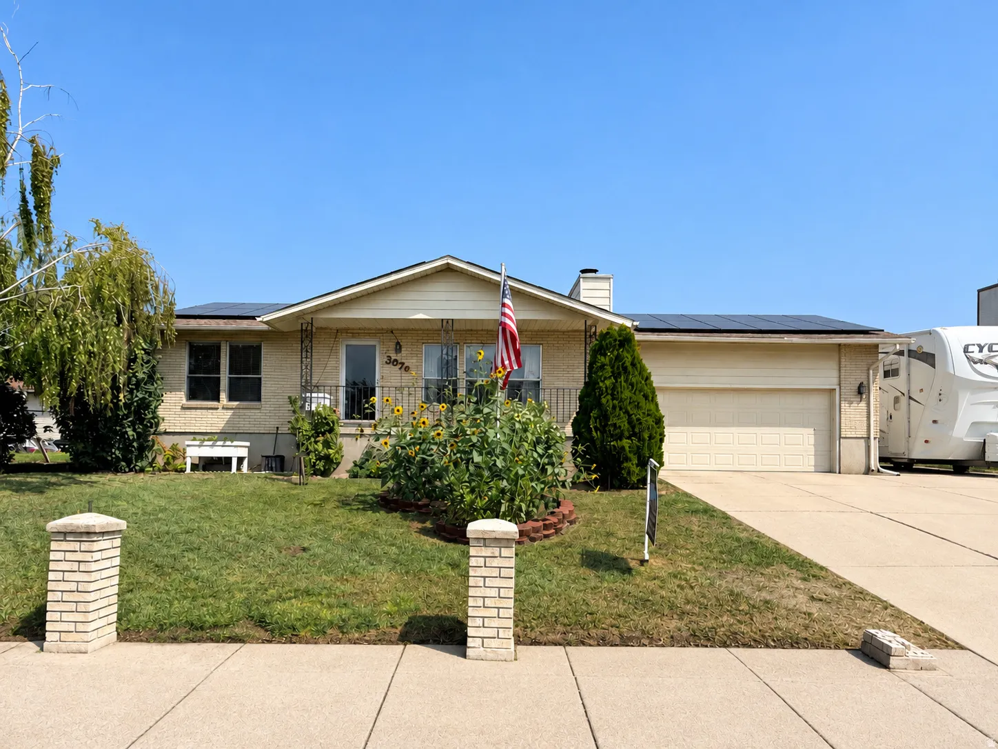 Brick veneer exterior with a covered entry, integrated solar panels, an attached garage, and a concrete driveway