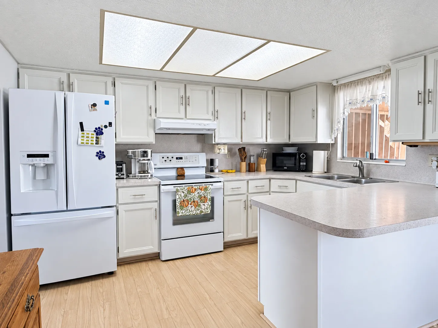 White cabinetry with satin nickel hardware, light-toned countertops, and wood-finish flooring