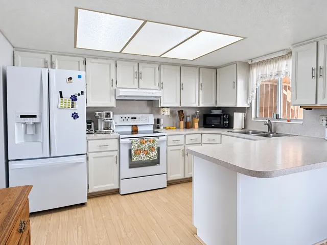 White cabinetry with satin nickel hardware, light-toned countertops, and wood-finish flooring