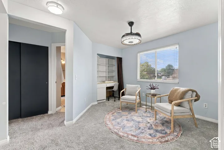 Carpeted room with a ceiling light fixture, large window, and built-in shelving with a desk
