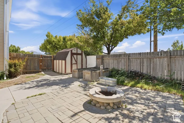 Paver patio with a stone fire pit, wood privacy fencing, a storage shed, and raised planting beds