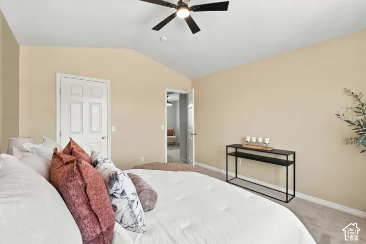 Vaulted ceiling with a black ceiling fan, light beige walls, and light-colored carpeting