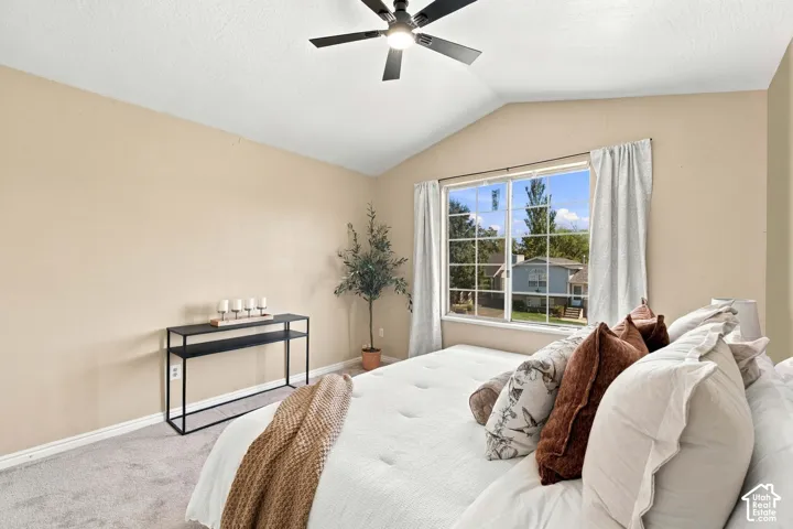 Vaulted ceiling with a ceiling fan, neutral wall tones, large window, and light-toned carpeting