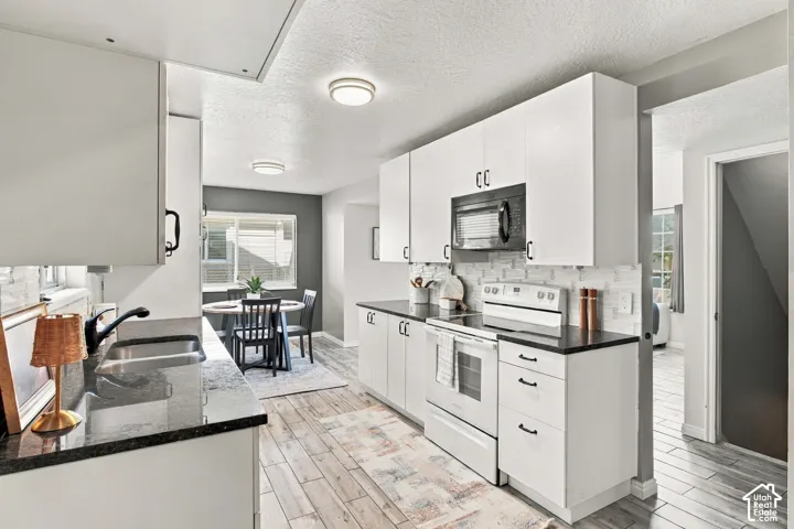White cabinetry with black hardware, dark countertops, a subway tile backsplash, and wood-finish flooring