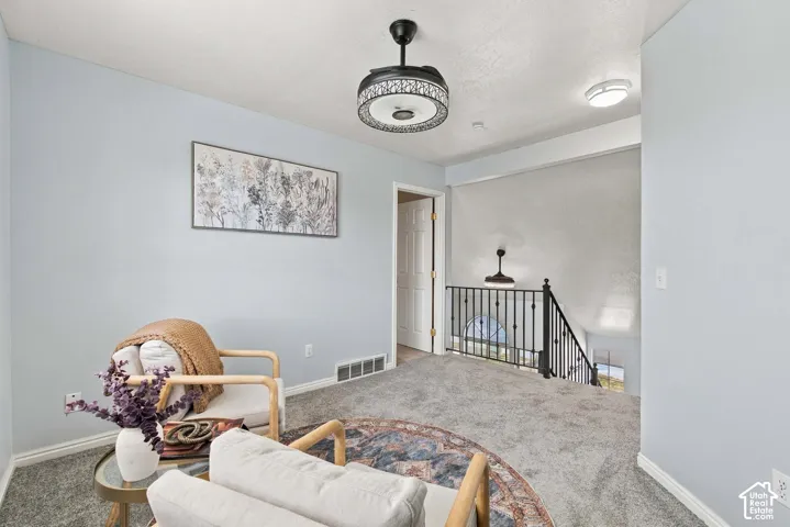 Textured gray carpeting, light blue wall paint, a ceiling-mounted light fixture with decorative metalwork, and a built-in metal railing on the staircase