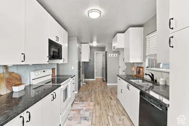 Galley kitchen featuring white cabinetry, dark countertops, wood-finish flooring, and integrated appliances