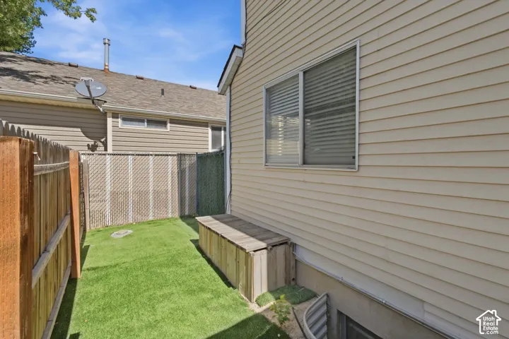 Enclosed backyard space featuring artificial turf, a wooden fence, chain-link fencing, and a wooden storage bench