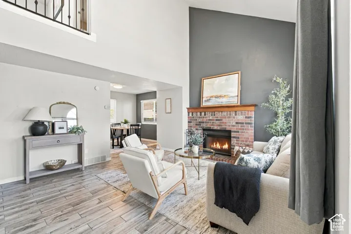 Living area featuring a brick fireplace with a wood mantle, a high ceiling, and wood-finish flooring