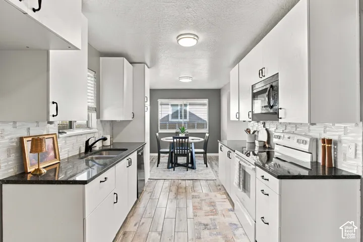 Galley kitchen featuring white cabinetry, dark stone countertops, wood-finish flooring, and a white subway tile backsplash