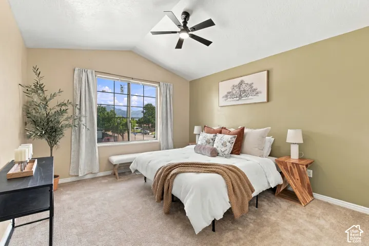 Vaulted ceiling with a ceiling fan, large window with grid pattern, carpeted flooring, and neutral wall tones