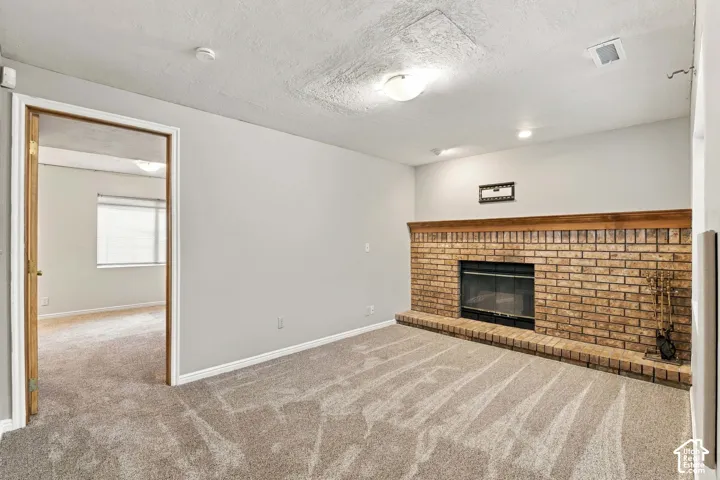 Brick fireplace with hearth, wood mantle, recessed lighting, and neutral carpet flooring