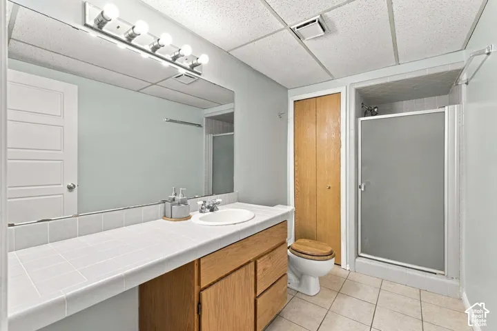 Wood-finish vanity with an integrated white sink, tiled countertop, and a full-width mirror