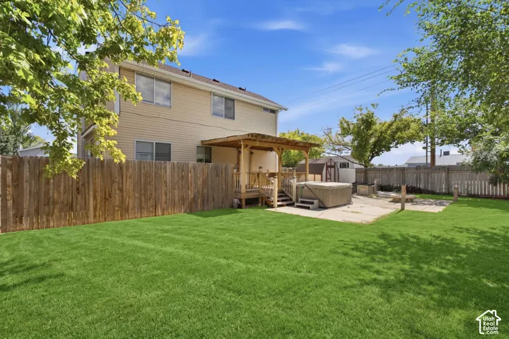 Expansive backyard featuring a wood privacy fence, concrete patio, and a wooden pergola over a raised deck