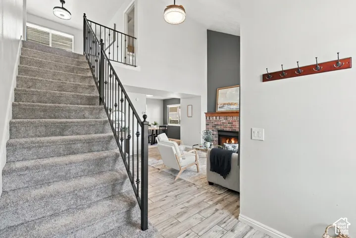 Staircase with wrought iron balusters, vaulted ceiling, wood-finish flooring, and brick fireplace with mantle