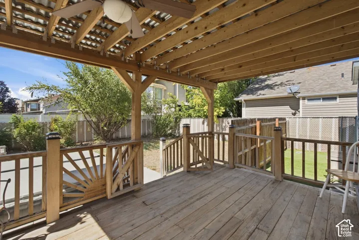 Expansive wooden deck featuring a pergola, decorative railing, ceiling fan, and staircase to the yard