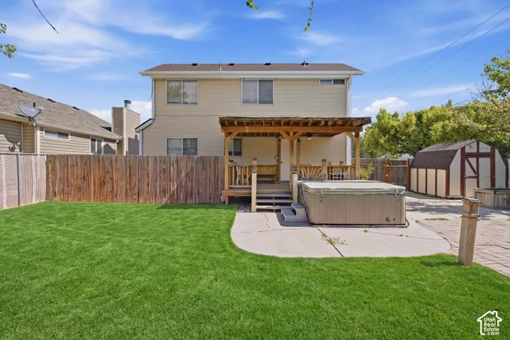 Expansive backyard featuring a manicured lawn, a concrete patio, a wooden pergola, a hot tub, and a storage shed