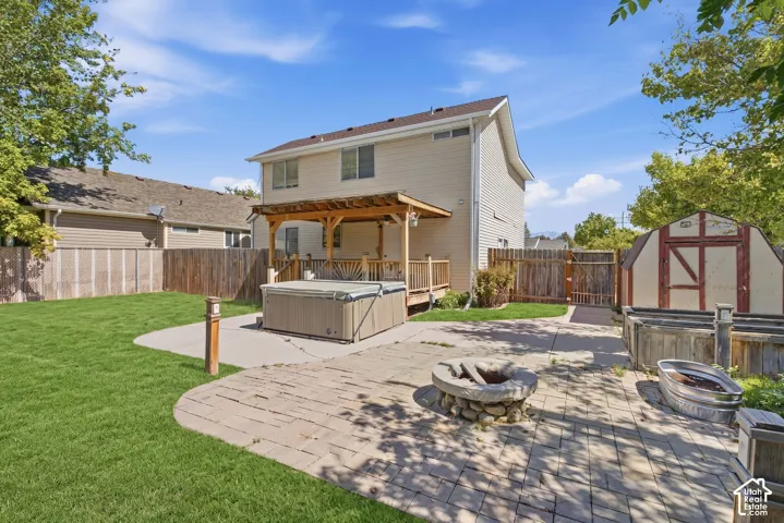 Expansive backyard featuring a covered deck, hardscaping with a stone fire pit, and a storage shed