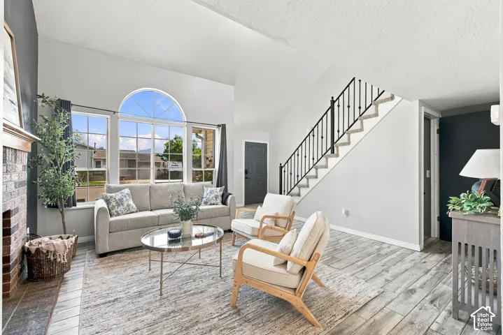 Vaulted ceilings, a full-height brick fireplace, a large arched window, wood-finish flooring, and a staircase with wrought iron balusters