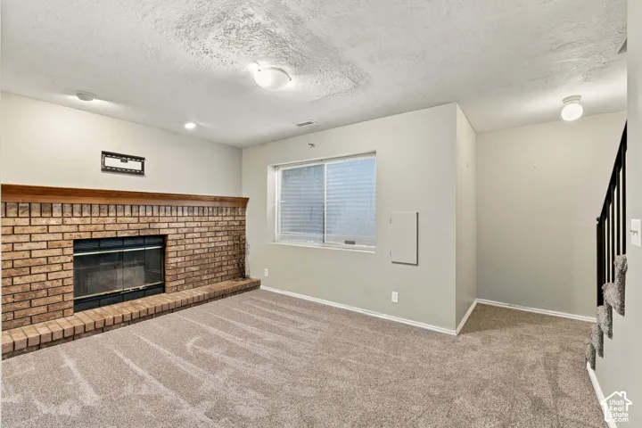 Brick fireplace with a wood mantle, neutral carpeting, and a single window