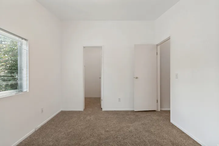 Neutral-toned carpeting, white painted walls, and a window with horizontal blinds
