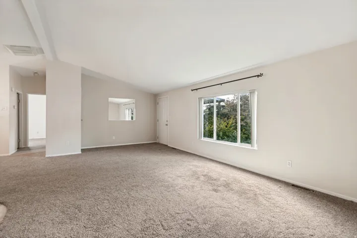 Spacious room with vaulted ceilings, neutral-toned carpeting, a built-in wall niche, and a large window