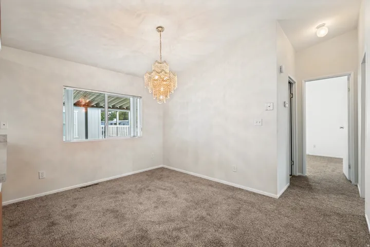 Textured ceiling, mounted chandelier, window with horizontal blinds, neutral-toned carpet, and interior doorway