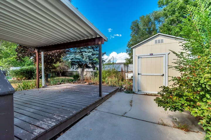 Covered deck with a corrugated metal roof, wood posts, and a separate storage shed