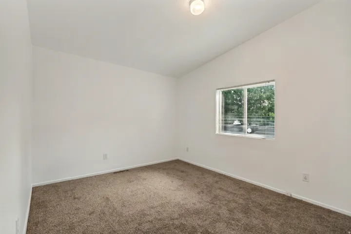 Vaulted ceiling above neutral carpeted flooring and white painted walls