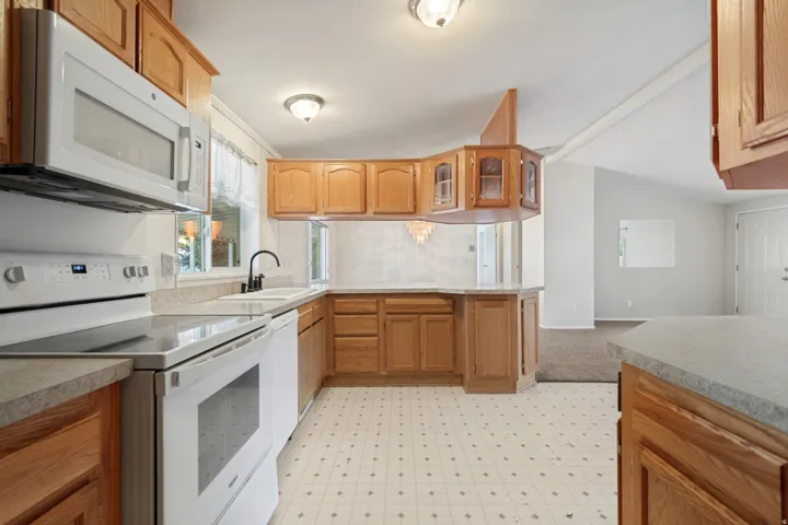 Kitchen featuring wood cabinetry, white appliances, a white sink with a gooseneck faucet, and patterned flooring