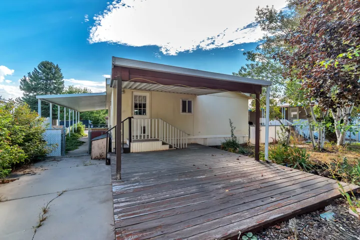 Covered outdoor deck with white railing, concrete walkway, and an extended covered structure