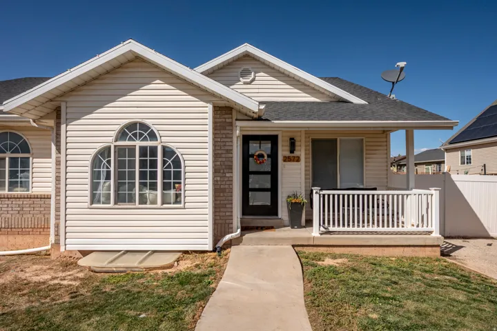 Exterior featuring light-colored siding, brick accent, an arched window, a covered porch, and a dark asphalt shingle roof