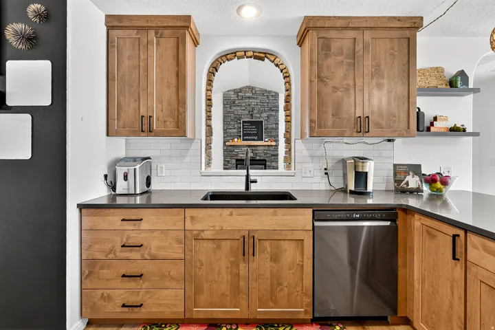 Kitchen featuring wood cabinetry, dark countertops, a tile backsplash, and a built-in stainless steel dishwasher