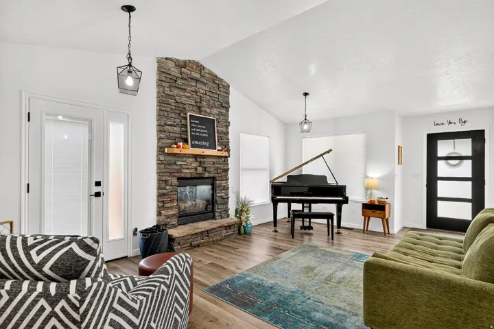 Vaulted ceilings, a stone-faced fireplace with hearth, wood-finish flooring, and a glass-paned entry door with a sidelight