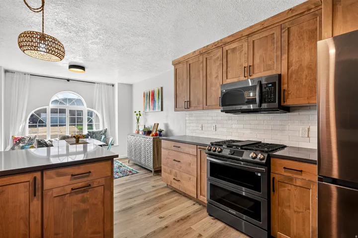 Wood-finish flooring, wood cabinetry with dark hardware, dark countertops, white subway tile backsplash, and a built-in window bench