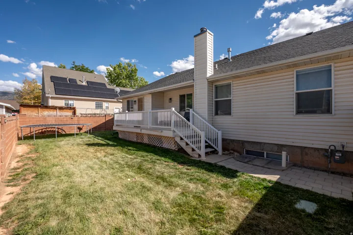 Backyard featuring a white composite deck with railings, an exterior chimney, a gravel roof, and a paved walkway