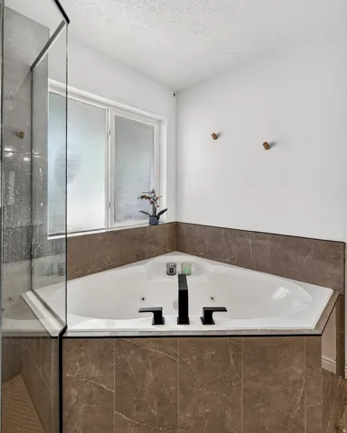 Corner soaking tub with matte black fixtures, surrounded by marbled-finish tile