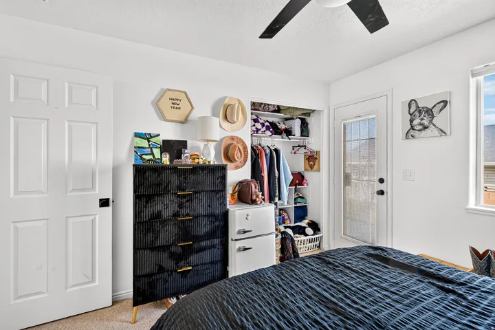 Ceiling fan with black blades, built-in closet shelving, white six-panel door, glass-paneled exterior door, and window with outdoor views