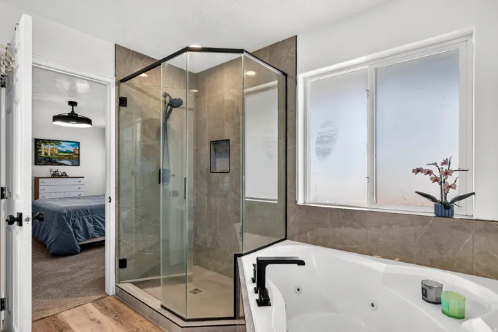 Corner glass shower enclosure with dark framing, large built-in soaking tub, and tiled surround