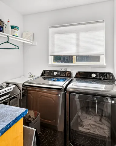 Dedicated laundry room with a utility sink, upper shelving, and a window with a cellular blind