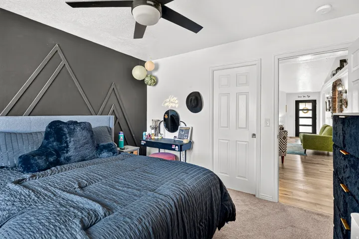 Carpeted bedroom with a decorative accent wall and ceiling fan