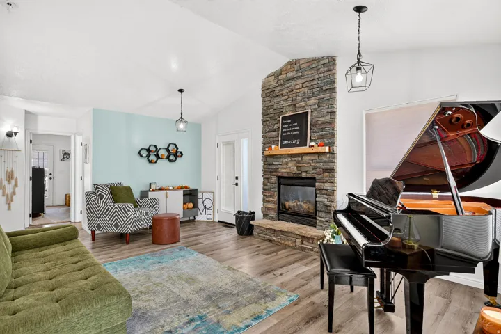 Vaulted ceiling, stone-clad fireplace with mantel, wood-finish flooring, and recessed lighting
