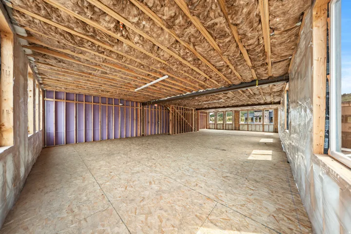 Exposed ceiling joists with insulation, framed interior walls, multiple window openings, and oriented strand board flooring