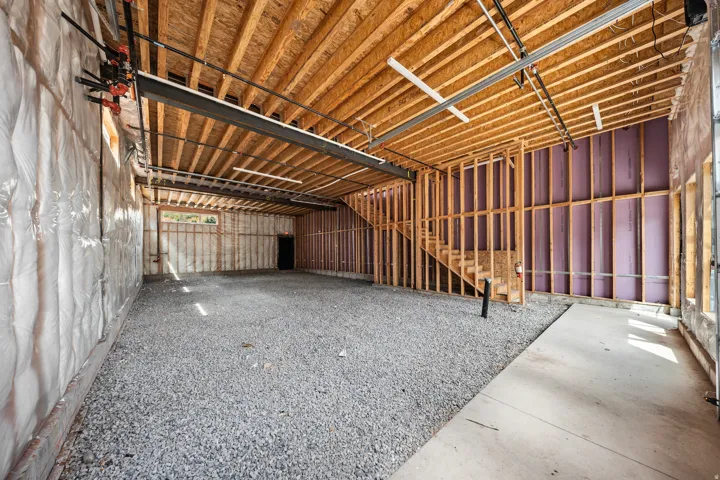 Unfinished basement featuring exposed wood framing, an open ceiling with visible joists, and a partial staircase