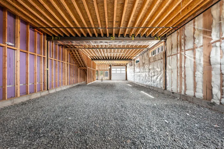 Exposed wood framing and ceiling joists, gravel floor, and visible insulation