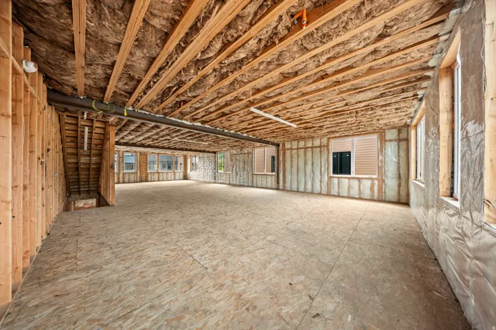 Spacious unfinished interior with exposed wood framing, ceiling insulation, and multiple windows