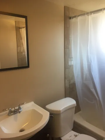 Integrated vanity sink with chrome faucet, framed mirror, and tile shower surround. Photo shown was taken prior to tenant occupancy and is provided for reference.