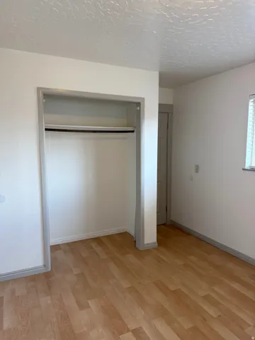 Wood-finish flooring with light-toned walls and a built-in closet featuring a hanging rod and shelf. Photo shown was taken prior to tenant occupancy and is provided for reference.